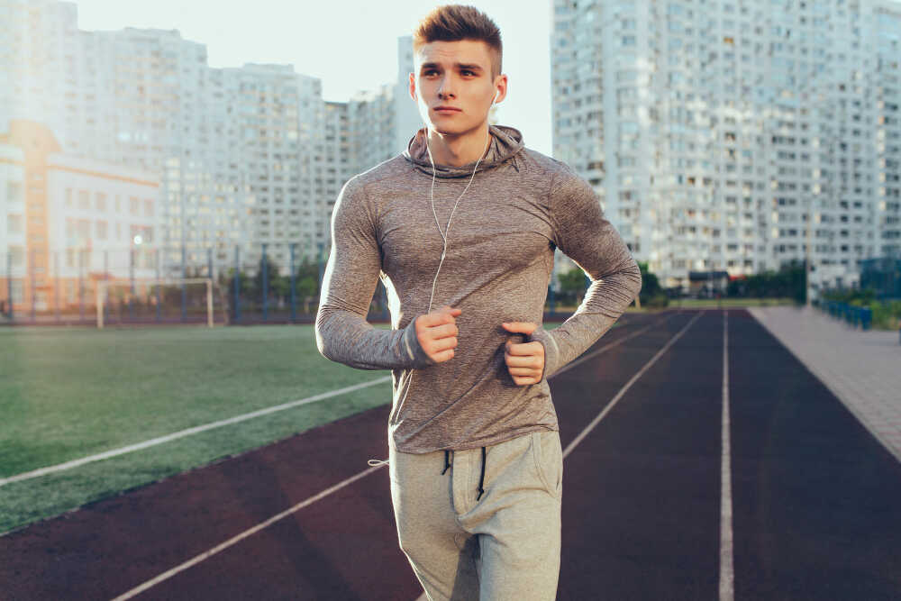 handsome-guy-gray-sport-suit-is-running-workout-morning-stadium-he-is-listening-music-through-headphones-looking-side